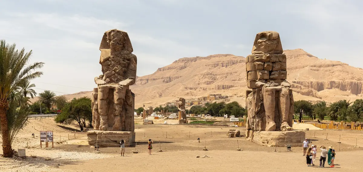Colossi of Memnon seated statues with palms and desert hills behind