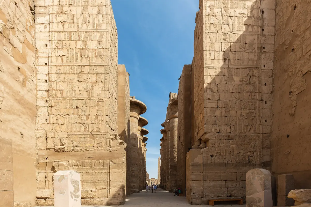 Narrow passage between two high pylon walls at Karnak under blue sky
