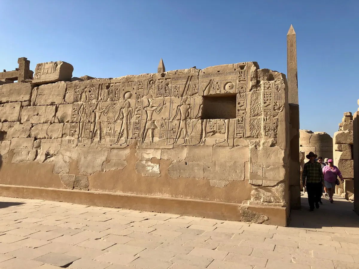 Relief wall with an obelisk visible behind it inside Karnak Temple