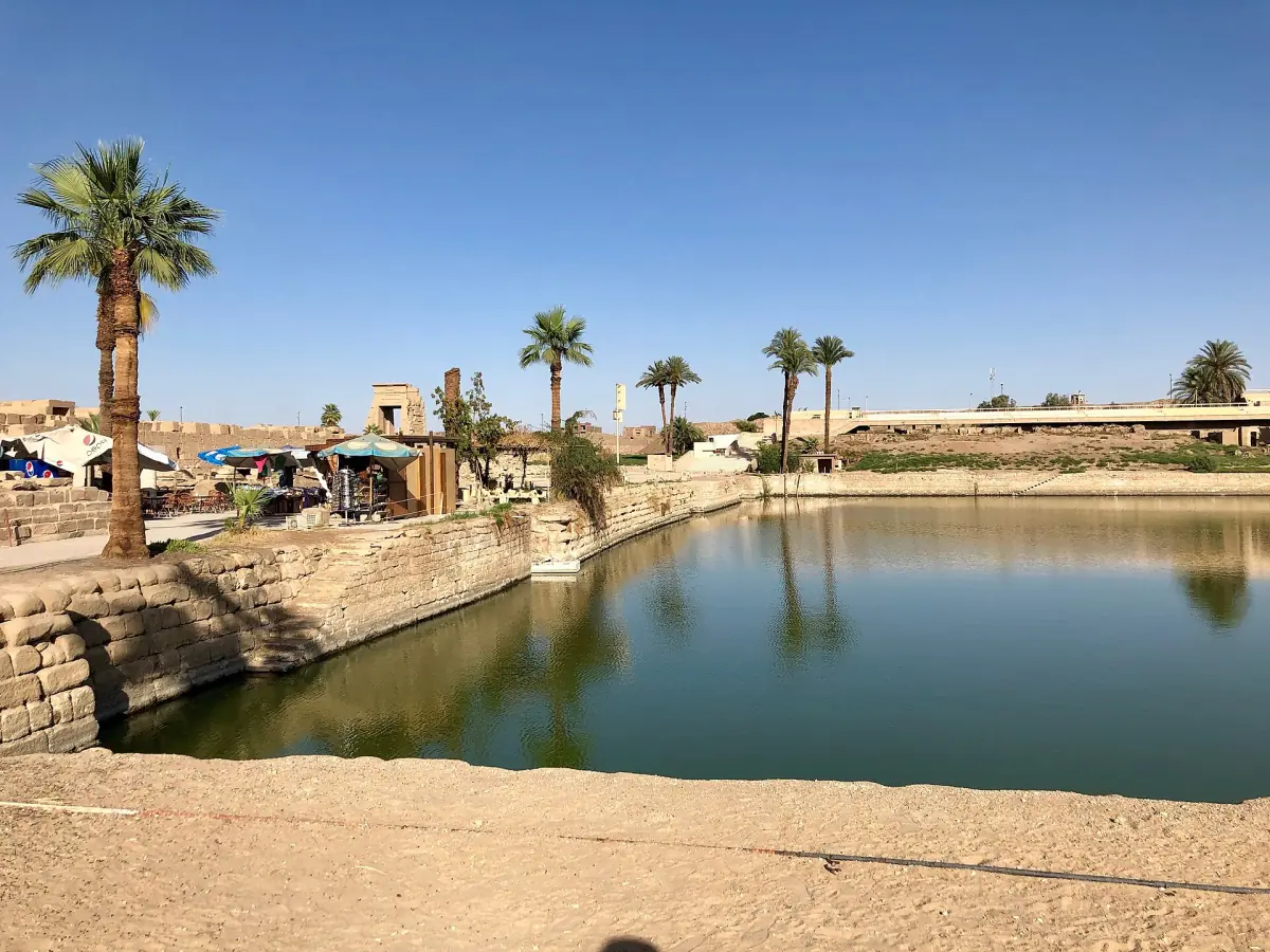 Still water of the Sacred Lake framed by a stone edge and palms
