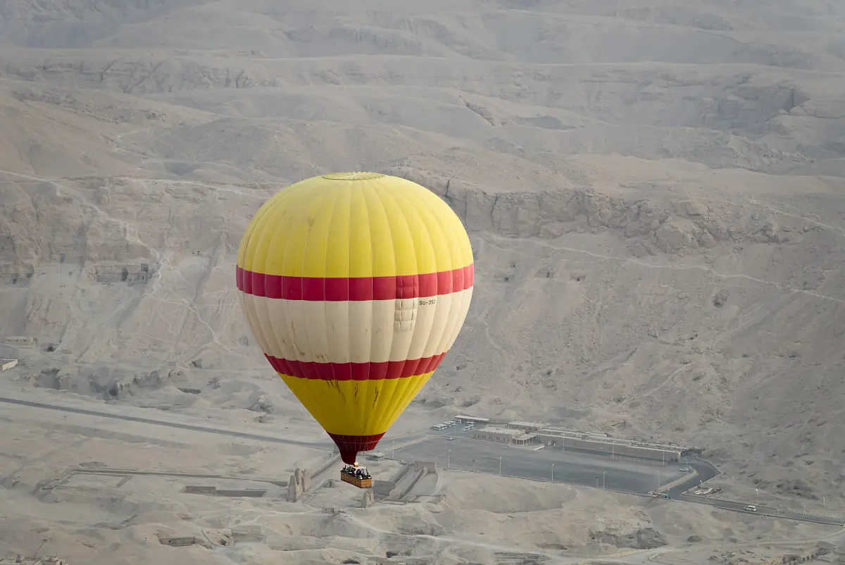 Yellow and red hot air balloon floating over the desert near the Valley of the Kings